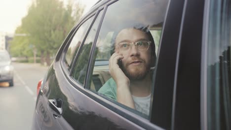 Atractivo-joven-cabalgando-sobre-un-asiento-de-un-coche-hace-una-llamada-de-teléfono,-conversaciones-con-clientes,-clientes-y-socios-de-negocios.-Cámara-de-disparo-desde-fuera-del-vehículo.