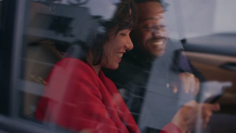 Beautiful-Woman-and-Her-Male-Partner-Riding-in-the-Back-Seat-of-a-Car,-they-Share-Smartphone-Screen-and-Talk-and-Have-Fun.-It's-Evening-in-the-Big-City.