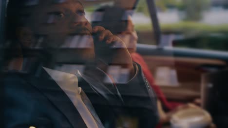 Beautiful-Businesswoman-and-Handsome-Businessman-Riding-on-the-Backseat-of-a-Car-in-the-Evening.-Man-Makes-a-Phone-Call,-Woman-Works-on-a-Laptop.-Camera-Shot-made-from-Outside-the-Car.