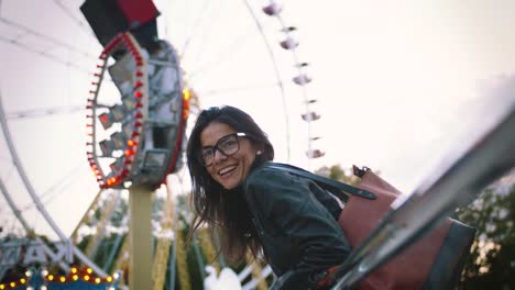 Young-stylish-woman-in-glasses-smiling-cheerfully-in-front-of-a-ferris-wheel-in-amusement-park
