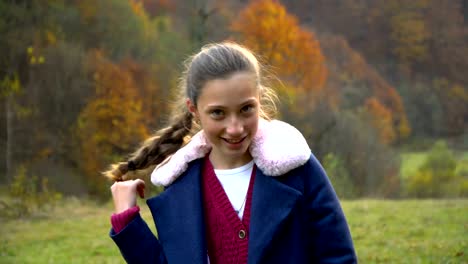 Una-hermosa-joven-está-de-pie-en-el-bosque-de-otoño,-mirando-a-la-cámara-y-sonriendo.-Ella-es-feliz.