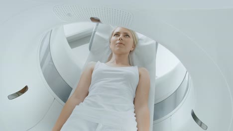 Female-Patient-Lying-on-a-CT-or-MRI-Scan,-Bed-is-Moving-inside-Machine-Scanning-Her-Body-and-Brain.-In-Medical-Laboratory-with-High-Tech-Equipment.-Elevated-Camera-Shot.