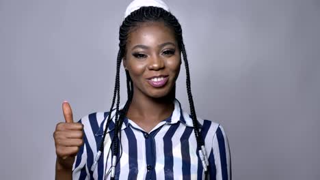 cute-happy-african-female-showing-like-gesture-and-looking-at-camera-with-nice-smile-while-standing-near-grey-wall