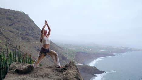 Mujer-meditando-en-pose-de-yoga-Guerrero-en-las-montañas-al-mar,-playa-y-roca.-Motivación-e-inspiración-para-montar-y-ejercicio.-Estilo-de-vida-saludable-al-aire-libre-en-la-naturaleza,-concepto-de-fitness.