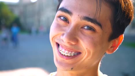 Cute-asian-man-close-up-smiling-in-braces-and-looking-at-camera-relaxed,-chill-mood,-outside,-sunshines