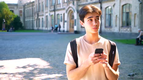 Smiley-happy-asian-guy-is-using-his-smartphone,-communication,-on-the-street-standing,-urban-mood,-cosy-sunny-place