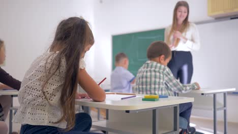 Retrato-de-sonriente-colegiala-en-el-escritorio-durante-la-lección-de-aprendizaje-en-aula-en-escuela-primaria-de-fondo-desenfocado