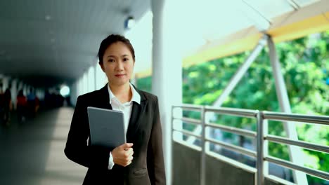 Young-working-woman-holding-laptop-walking-straight-ahead-on-bridge