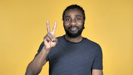 Victory-Sign-by-Casual-African-Man-Isolated-on-Yellow-Background