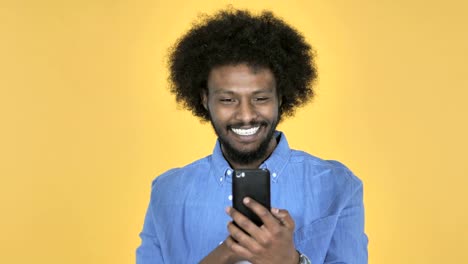 Afro-amerikanischer-Mann-begeistert-für-den-Erfolg-bei-der-Verwendung-von-Smartphone-auf-gelbem-Hintergrund