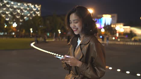 hübsche-junge-Asiatin-mit-Handy-in-der-Stadtstraße-in-der-Nacht,-4k