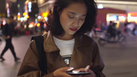 pretty-young-asian-woman-using-mobile-phone-in-the-city-street-at-night,-4k