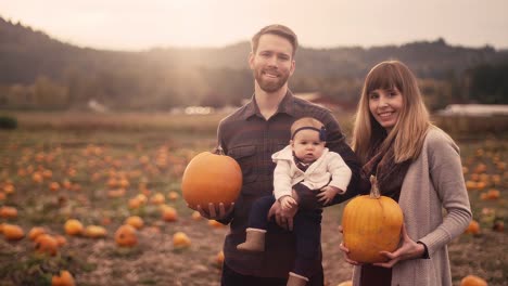 Retrato-de-una-joven-familia-en-una-parcela-de-calabaza,-madre-y-padre-la-celebración-de-calabazas,-con-resplandor-del-objetivo