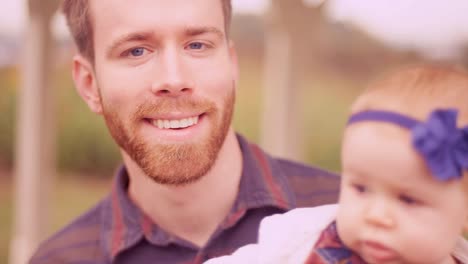 A-young-man-playing-with-his-baby-daughter-under-a-gazebo,-and-smiling-at-the-camera,-close-up