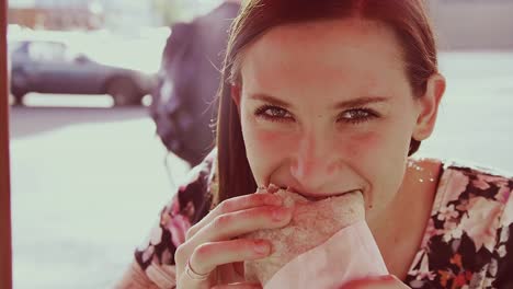 A-beautiful-girl-at-an-outdoor-table-eating-a-burrito-and-laughing,-slow-motion