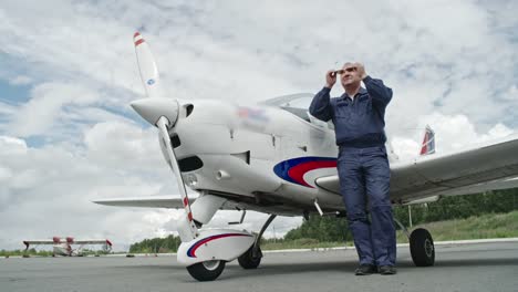 Mature-Pilot-in-Sunglasses-Standing-before-Plane