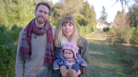 Retrato-de-una-joven-madre,-padre-y-su-niña-en-una-granja-de-árboles-de-Navidad