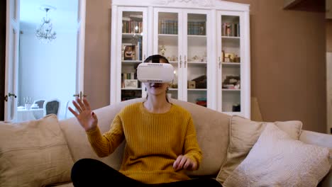 Schöne-junge-Frau-sitzt-auf-dem-Sofa-im-Wohnzimmer-und-VR-Kopfhörer-verwenden.-4K