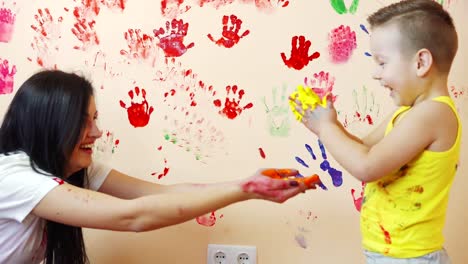 Happy-mother-and-her-cute-boy-having-fun-together-leaving-their-colorful-handprints-on-the-wall.-Young-happy-family.-Mother-and-child-concept