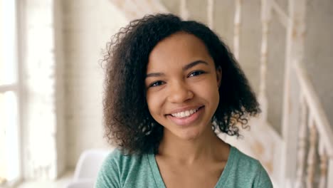 Closeup-portrait-of-beautiful-african-american-girl-laughing-and-looking-into-camera.-Teenager-show-emotions-from-serios-face-to-laugh-at-home