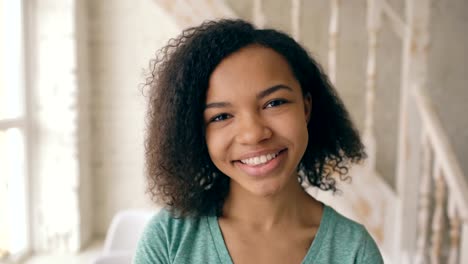 Nahaufnahme-Porträt-von-schönen-afrikanischen-amerikanischen-Mädchen-lachen-und-Blick-in-die-Kamera.-Teenager-zeigen-Emotionen-von-serios-Gesicht-zu-Lachen-zu-Hause