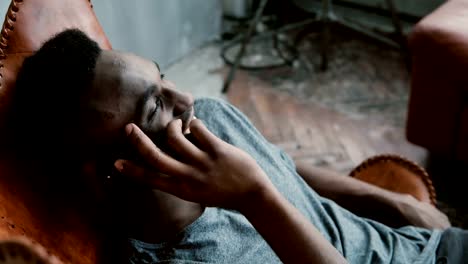 Portrait-of-young-African-man-is-sitting-in-the-chair.-Male-using-Smartphone,-talking,-smiling-and-laughing