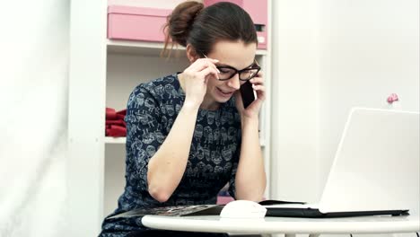 Jóvenes-atractiva-mujer-diseñadora-con-ordenador-portátil-y-hablando-por-teléfono-móvil-en-la-fabricación-de-oficina-estudio