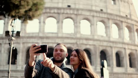 Feliz-pareja-joven-con-smartphone-para-tomar-fotos-selfie-cerca-de-Coliseo-de-Roma,-Italia.-Hombre-y-mujer-tienen-vacaciones