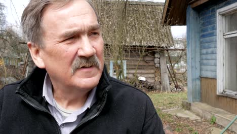 An-elderly-man-with-a-mustache-smokes-in-the-street-near-the-old-house.-Dressed-in-a-black-sweater