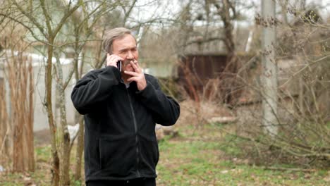 Ein-älterer-Mann-mit-einem-Schnurrbart-raucht-und-spricht-am-Telefon-in-der-Straße.-Die-alten-Häuser-liegen-hinter-uns.-Die-schwarze-Jacke