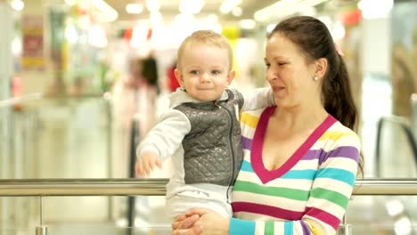 Mom-keeps-a-pretty-blond-son-in-his-arms-in-the-mall.-Against-the-background-people-go-shopping