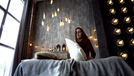 Pretty-brunette-woman-in-dress-sits-on-bed-and-poses-in-studio