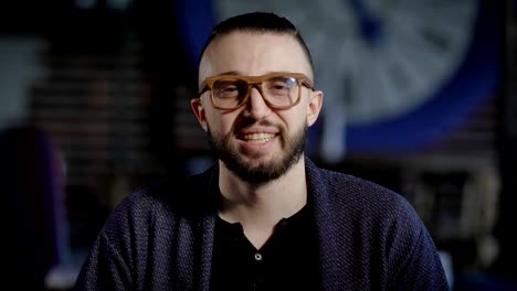 Portrait-of-handsome-positive-hipster-looking-at-the-camera-and-smiling.-Stylish-man-in-blue-jacket-and-fashionable-eyeglasses-staring-before-him-trying-to-be-serious,-removing-his-eyes-and-laughing