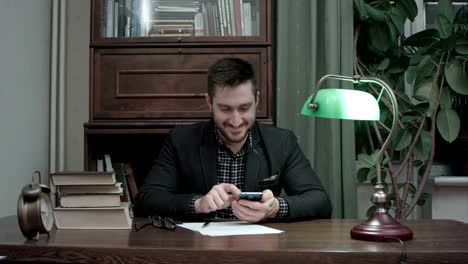 Young-writer-at-his-desk-happily-messaging-on-mobile-phone