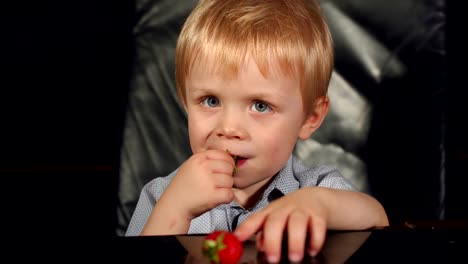 Little-boy-eating-strawberries-on-black-background