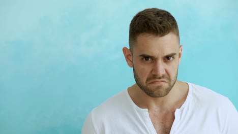 Portrait-of-angry-young-man-looking-into-camera-on-blue-background