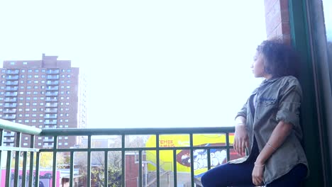 Ethnic-girl-with-afro-looking-out-at-the-city-from-her-balcony