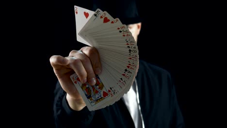 Professional-Street-Magician-in-a-Cap-Performing-Sleight-of-Hand-Card-Tricks,-Fan-Out-Cards,-Spinning-One-Card-on-a-Finger.-Background-is-Black.