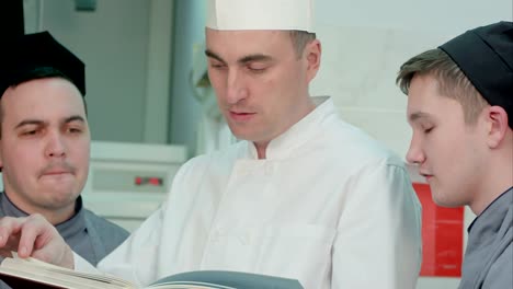 Head-chef-holding-recipe-book-and-discussing-something-with-his-trainees