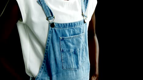 Androgynous-man-in-dungaree-posing-against-black-background