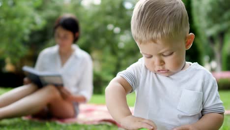 Boy-plays-with-toy-and-mom-reads-book-on-blurred-background