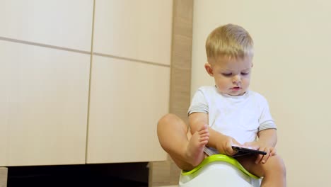 Cute-niño-pequeño-juega-con-teléfono-sentado-en-el-orinal