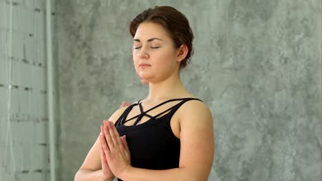 Portrait-of-young-beautiful-athletic-girl-practicing-indoor-yoga-with-closed-eyes-and-palms-in-namaste-gesture