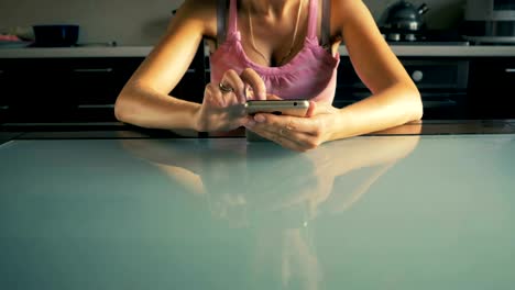 Dolly-the-young-girl-sits-at-the-table-and-read-on-the-smartphone-in-the-kitchen-at-home.