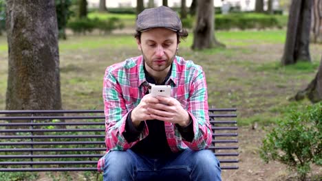 young-man-sitting-on-a-bench-at-the-park,-chat-happily-with-his-smartphone