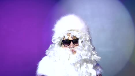 Santa-Claus-in-sunglasses-looking-at-the-camera-at-party.-Multicolored-lighting-background