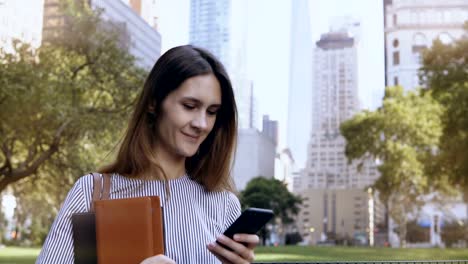 Young-happy-businesswoman-standing-in-financial-district-of-New-York,-USA-and-using-the-smartphone-as-mobile-office