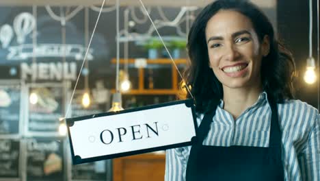 Hermosa-Cafe-joven-propietario-muestra-escaparate-de-cerca-abiertos-y-Bienvenidos-nuevos-clientes-en-su-moderno-aspecto-elegante-cafetería-los-bancos.