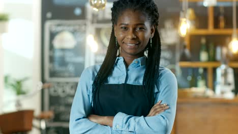 Schöne-African-American-Cafe-Besitzer-Stand-mit-verschränkten-Armen-und-einem-Lächeln-in-ihrem-stilvollen-Kaffeehaus.