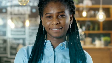 Beautiful-African-American-Cafe-Owner-Walking-into-Focus-while-in-the-Background-Her-Stylish-Coffee-House-Shines-with-Lights.